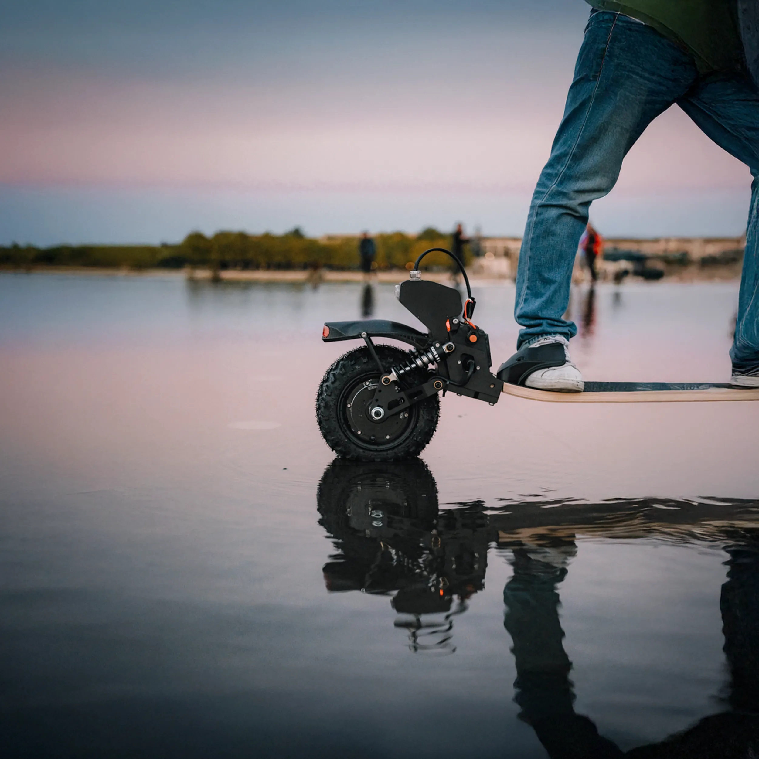 Skateboard électrique Sternboard trois roues reflété dans eau calme au coucher de soleil
