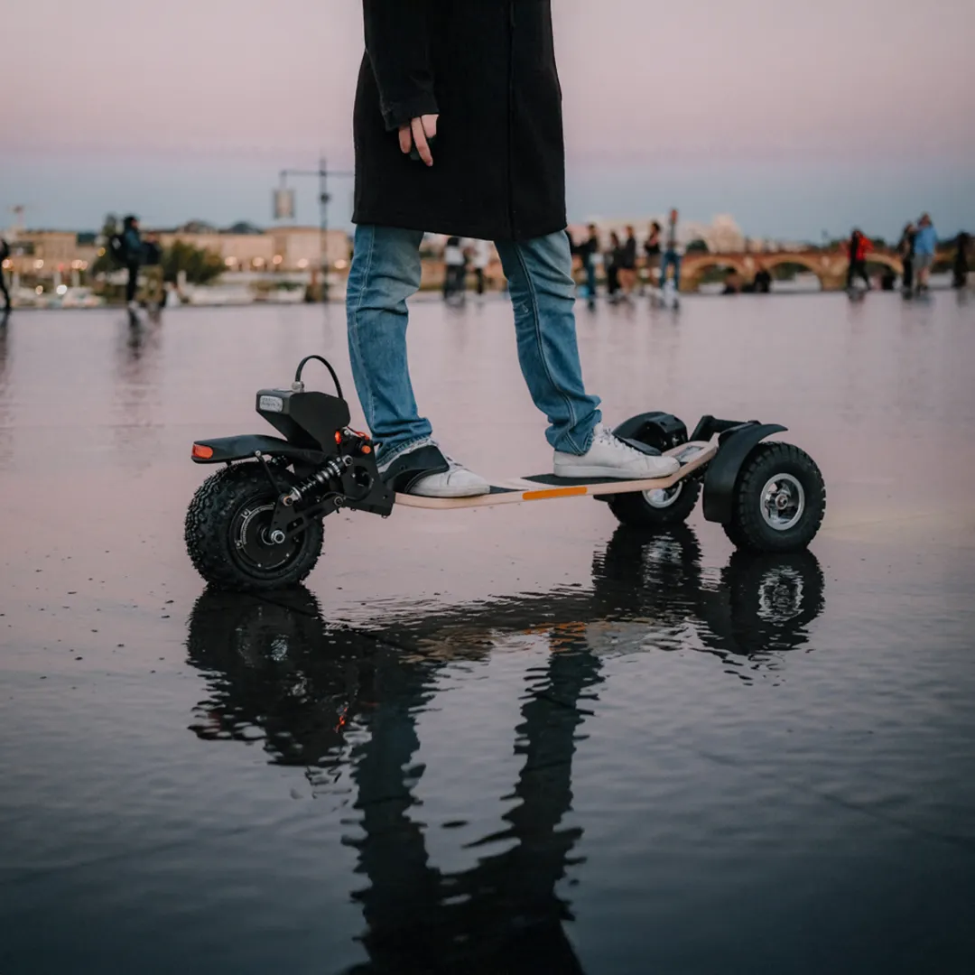Skateboard électrique Sternboard trois roues avec batterie au dos en utilisation urbaine sur surface mouillée