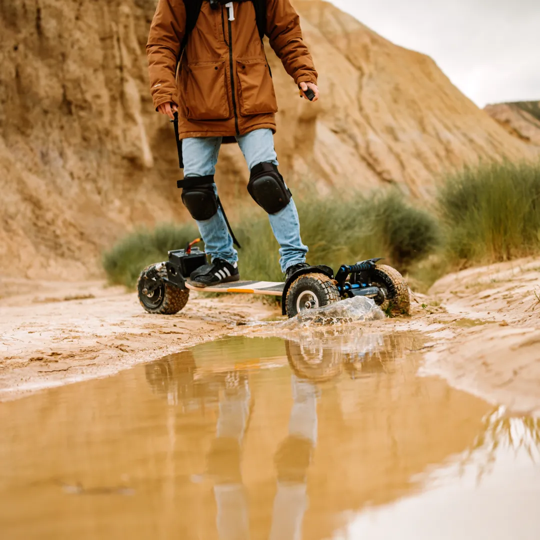 Rider Sternboard équipé genouillères traversant grande flaque boueuse avec skateboard électrique étanche