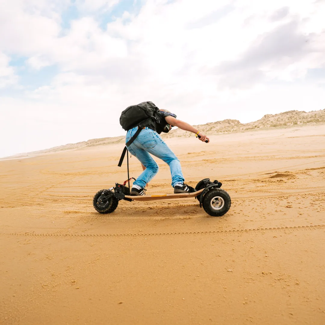 Rider Sternboard effectuant virage dynamique sur plage avec skateboard électrique trois roues tout-terrain