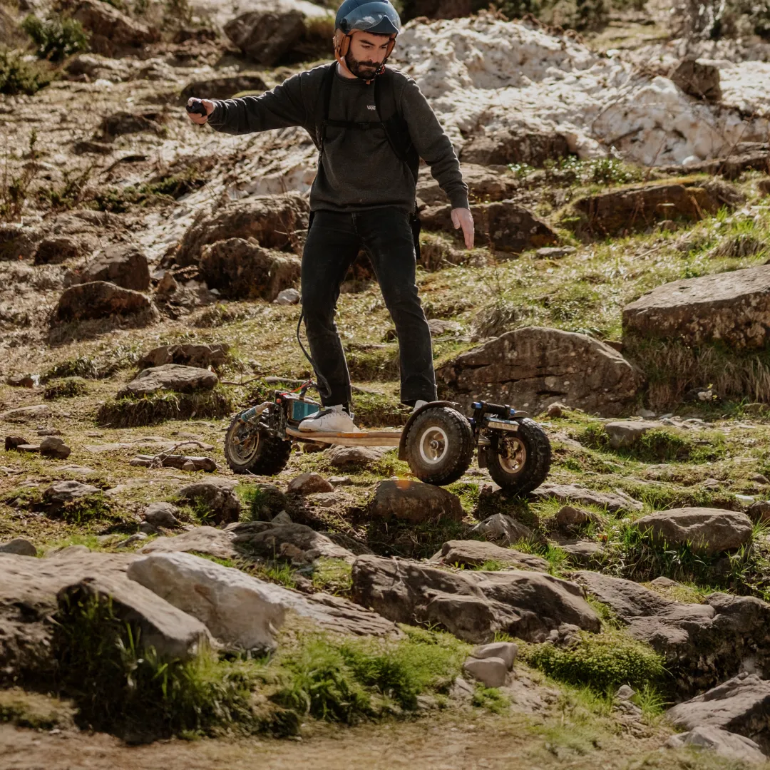 Rider Sternboard équipé casque franchissant terrain rocheux accidenté avec skateboard électrique trois roues